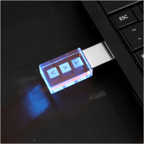 A 3D crystal flash drive with a transparent blue casing, plugged into a laptop's USB port, emitting a soft glow.