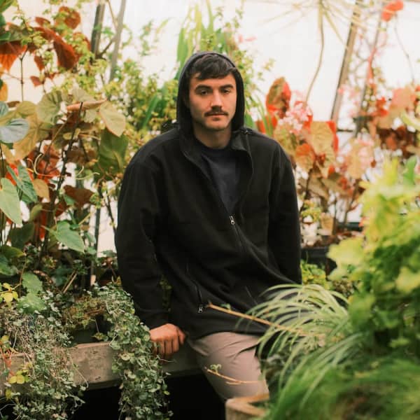A black windproof fleece jacket with a full zip and hood, displayed against a lush green plant backdrop.