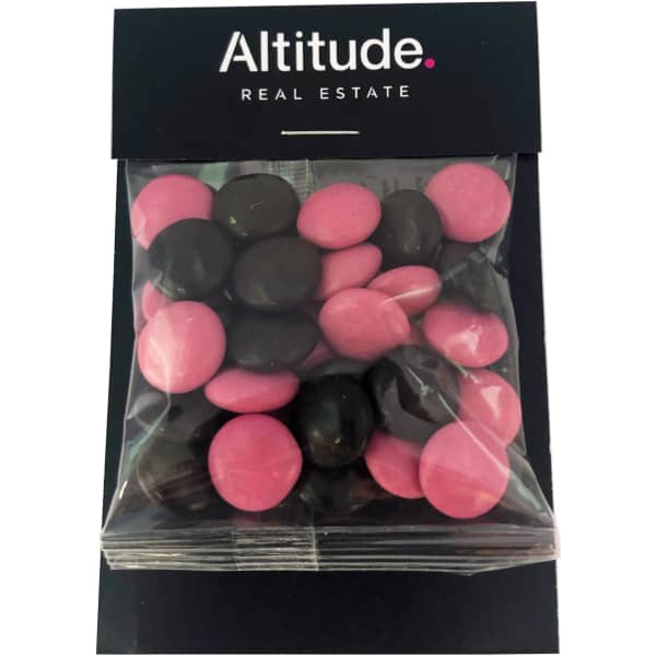 A bag of choc beans featuring pink and dark brown candies, presented in a clear packaging with a branded header.