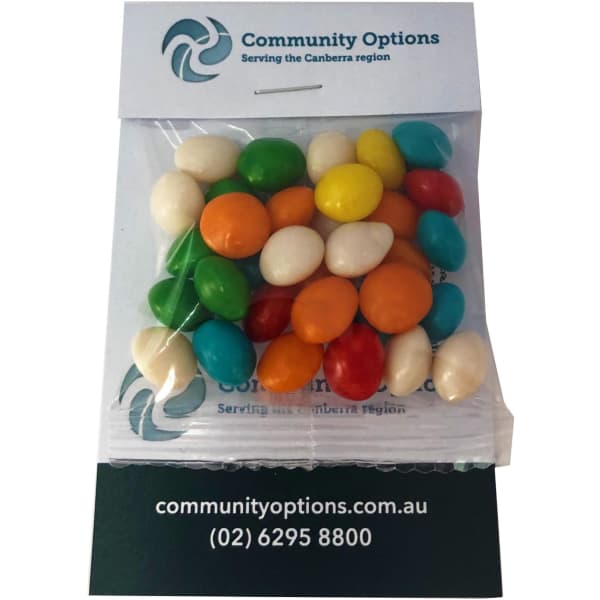 A clear bag filled with colourful chewy fruit candies, including green, orange, yellow, blue, and white pieces, placed on a card with a logo.