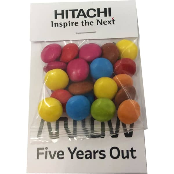 A bag of multi-coloured chocolate beans, featuring pink, blue, yellow, orange, and brown candies, with branding on the packaging.