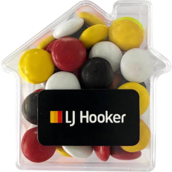 Acrylic house-shaped container filled with colourful choc beans in red, yellow, white, and black. Features a logo.