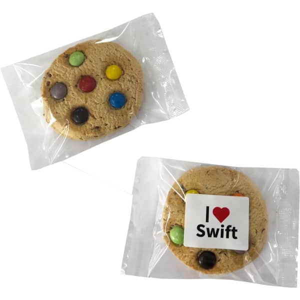 A cookie featuring colourful chocolate buttons, wrapped in clear packaging with a logo.