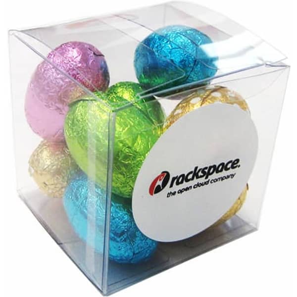 A clear cube containing mini Easter eggs in blue, pink, green, gold, and silver foil, with a logo on one side.
