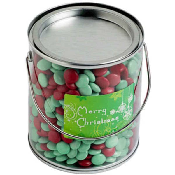 A metal bucket filled with red and green chocolate beans, featuring a festive label on the front.