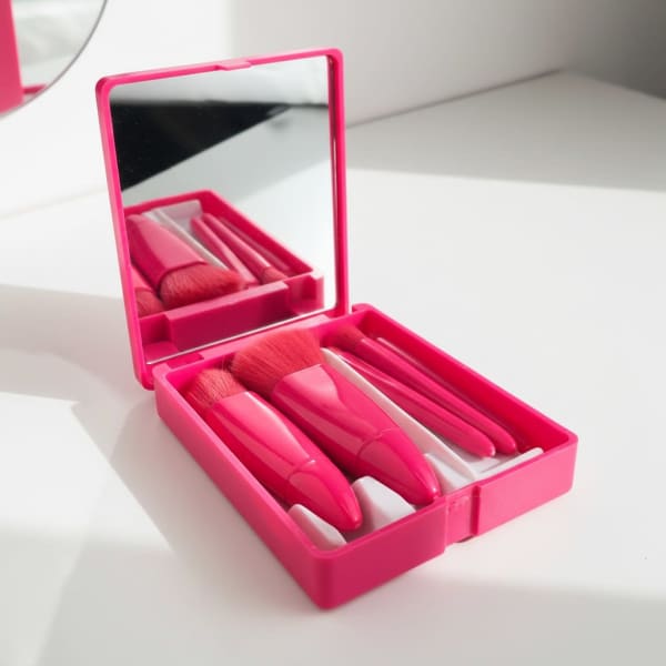 A pink plastic box containing five makeup brushes and a mirror inside.