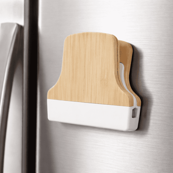 A bamboo fridge magnet clip with a wooden back and white plastic base, attached to a stainless steel fridge.