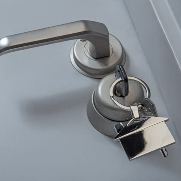 A silver house-shaped key ring attached to a silver door handle, set against a grey background.