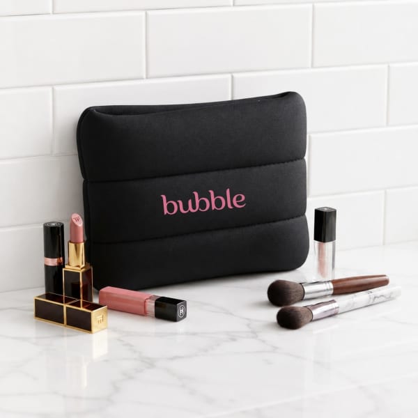 A black neoprene cosmetic bag with pink branding, surrounded by various lip products and makeup brushes.