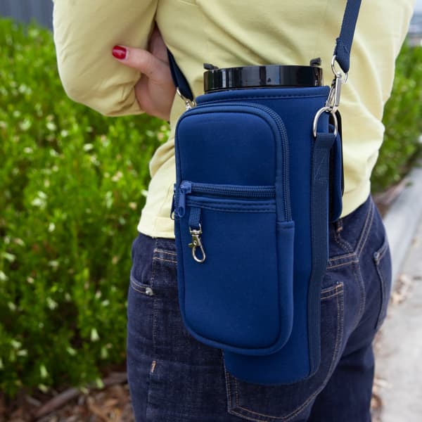 A drink bottle carrier in navy neoprene, featuring a zippered pocket and an adjustable strap, worn on a person's waist.