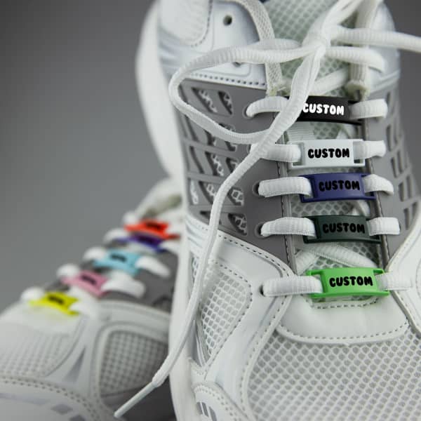 A pair of white sneakers featuring colourful luxury shoelace charms with a custom design.