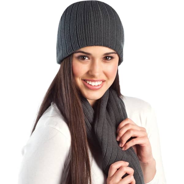 A cable knit beanie in grey worn with a matching scarf, displayed on a smiling model.