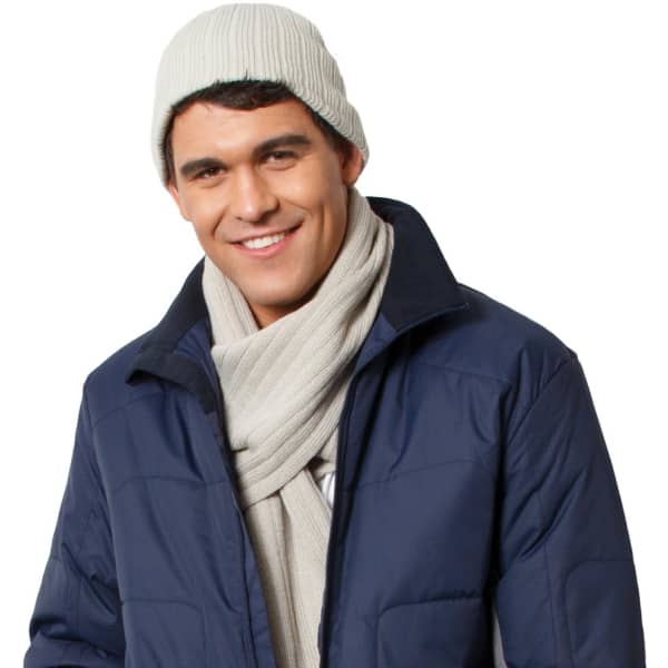 A man wearing a light grey cable knit beanie and a matching scarf, paired with a navy jacket. The image has a logo present.