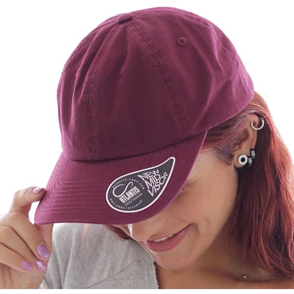 A maroon Dad Hat featuring a curved visor and a logo on the side, worn by a person with red hair.