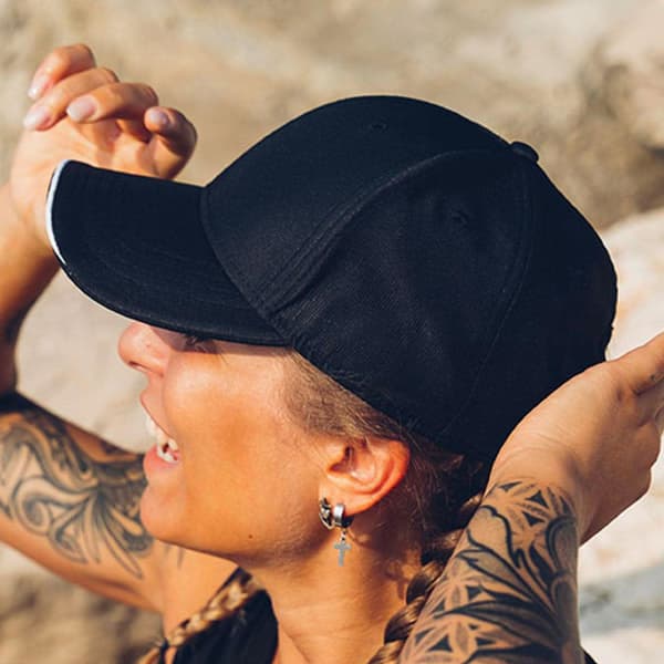 A black cap with a curved brim, worn by a person with tattoos, showcasing a side view.