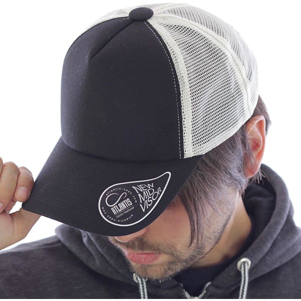 A black and white trucker cap with a mesh back and a logo on the front, worn by a person.