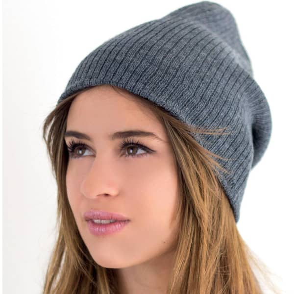 A grey beanie with a ribbed texture, worn by a model with long hair, featuring a logo on the side.