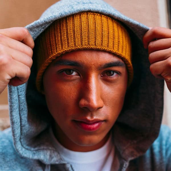 A young man wears a mustard yellow beanie under a grey hoodie, showcasing the headwear's textured ribbing.