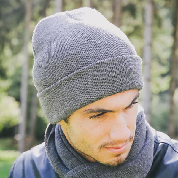 A grey beanie was worn by a man, featuring a snug fit and a subtle logo, set against a natural backdrop.