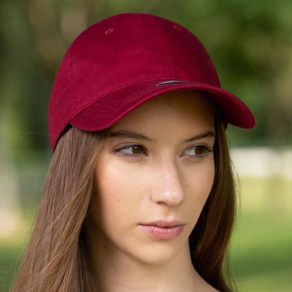 A burgundy cap with a curved brim and a logo on the front, worn by a person outdoors.