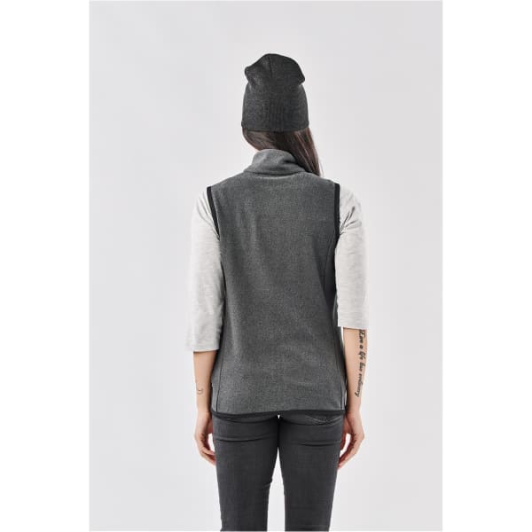 A dark grey beanie worn by a person with long hair, standing in a grey outfit, viewed from the back.