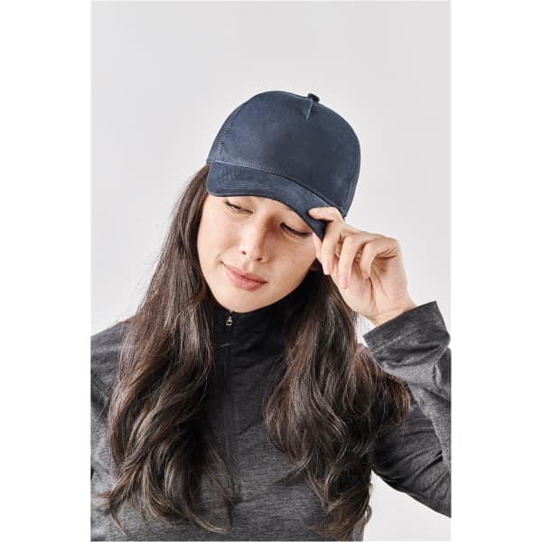 A navy trucker cap with a curved brim, featuring a logo on the front, worn by a woman with long hair.