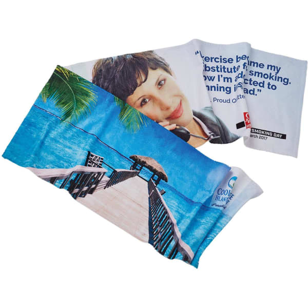 A sublimation sports towel with a vibrant beach scene and a person’s image, featuring blue and white colours.