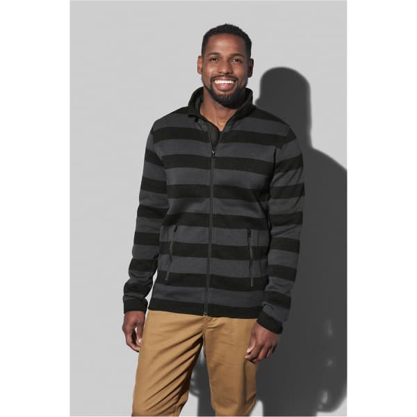 A black and grey striped fleece jacket with a zip, worn by a smiling man. The background is a simple grey.