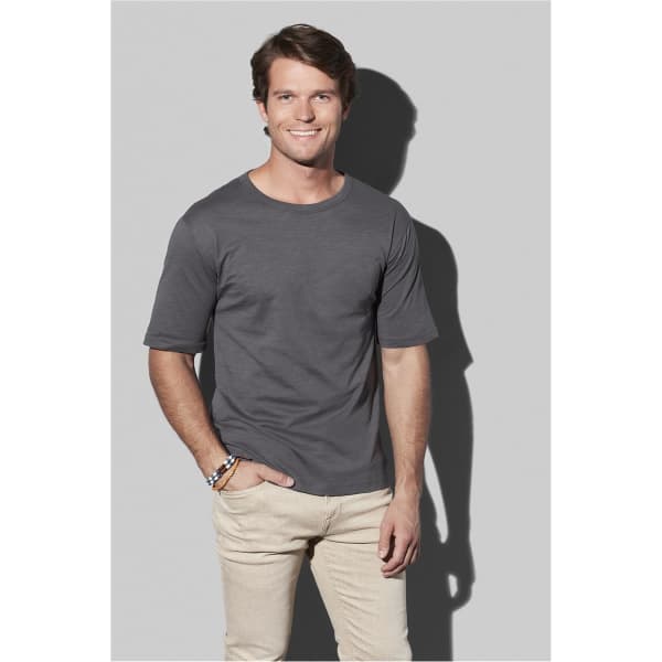 A grey organic slub T-shirt displayed on a smiling model, standing against a light grey background.