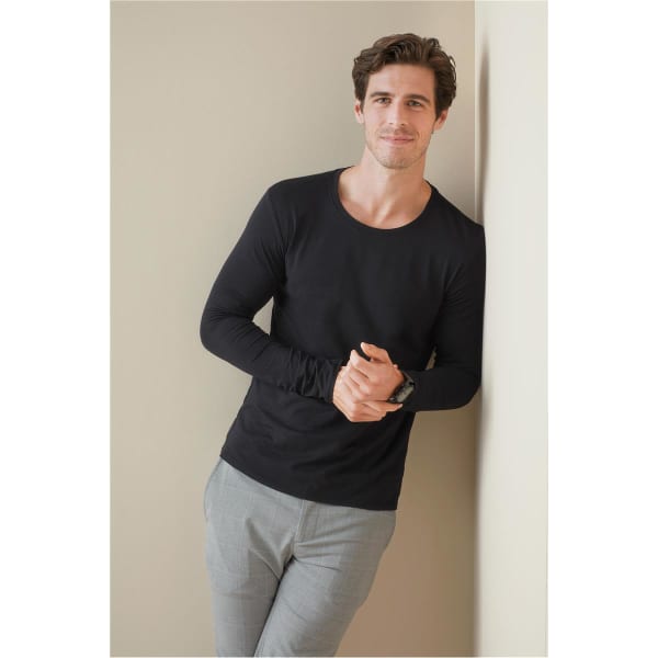 A black long sleeve shirt displayed on a man leaning against a wall, paired with light-coloured pants.