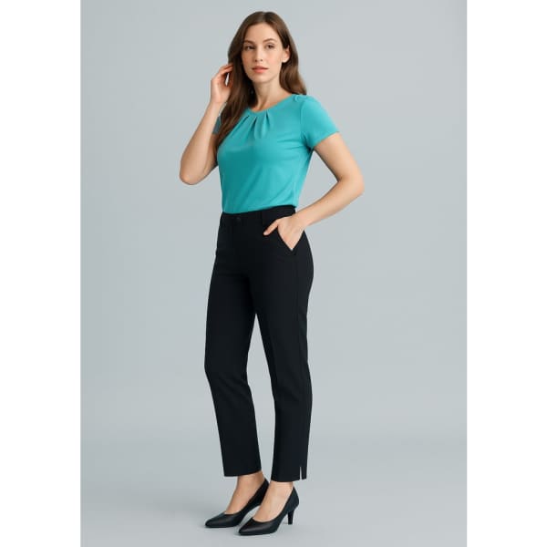 A woman wearing a turquoise top and black slim leg pants, standing against a light grey backdrop. The pants feature pockets and a logo.