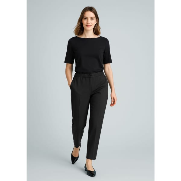 A woman wearing black slacks and a black top, walking confidently with her hands in the pockets of the pants.