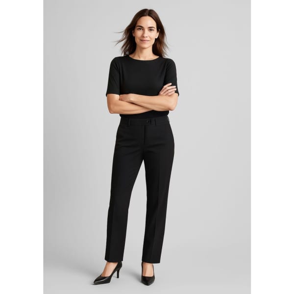 A woman wears black comfort wool stretch relaxed pants paired with a black top and high heels, standing confidently.