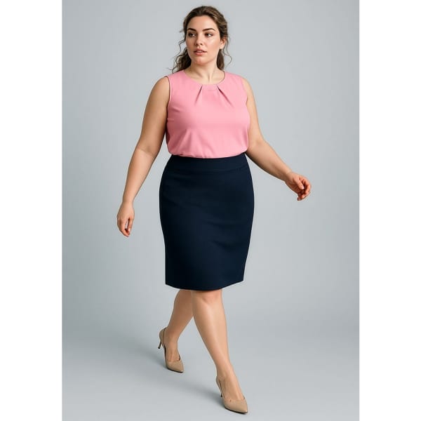 A woman models a fitted navy skirt paired with a pink top, wearing neutral heels and standing against a light grey background.