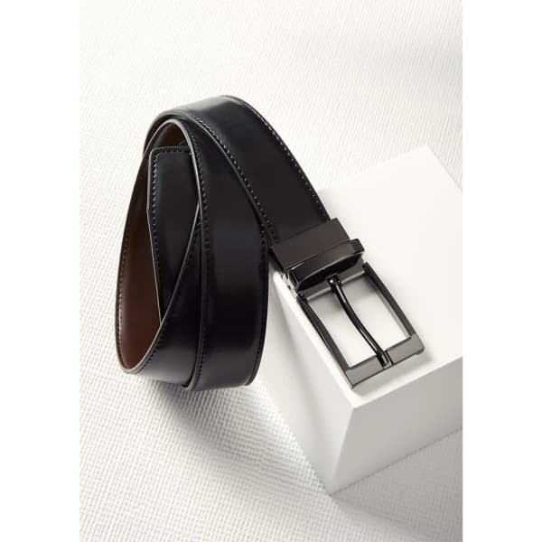 A reversible men's leather belt in black with a metallic buckle, displayed on a neutral surface.