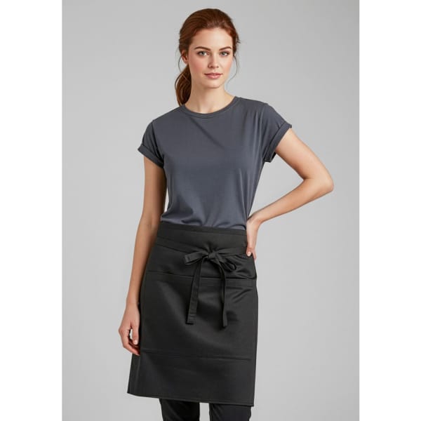 A woman in a grey top is wearing a black short-waisted apron with a tied bow at the waist. The apron has a logo.