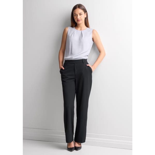A woman stands wearing soft stretch black pants paired with a light grey top. She has long brown hair and is posing against a neutral backdrop.