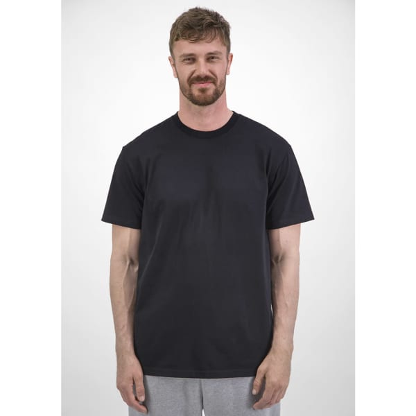 A man stands wearing a plain black short sleeve tee, with a neutral background. The tee features a logo.
