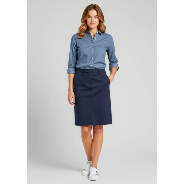 A woman stands wearing a navy skirt paired with a blue shirt and white sneakers, featuring a logo.
