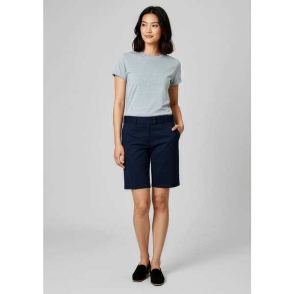 A woman is wearing navy dress shorts paired with a grey t-shirt, standing against a plain background.