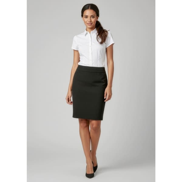 A knee-length women's skirt in black, paired with a white button-up shirt and black heels. The model has long hair styled casually.