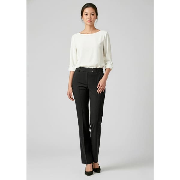 A woman stands wearing black slacks and a white top, with a logo visible on the garment.