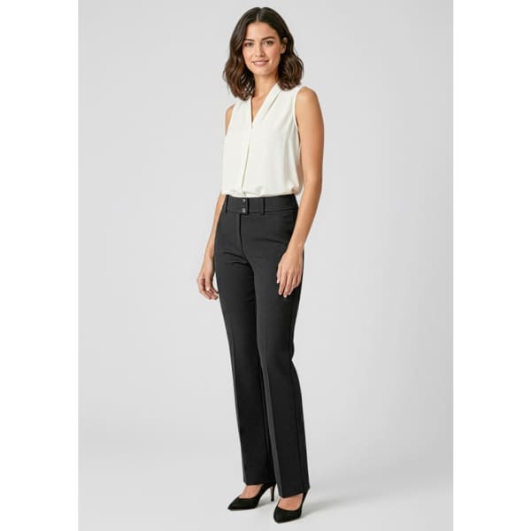 A woman stands wearing black tailored slacks and a white sleeveless top, complemented by black heels.
