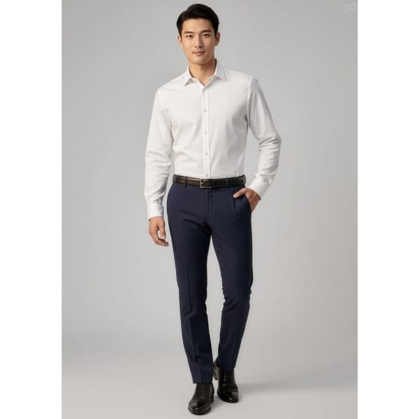 A man models navy classic slim pants paired with a white shirt and black belt, standing in a neutral backdrop.