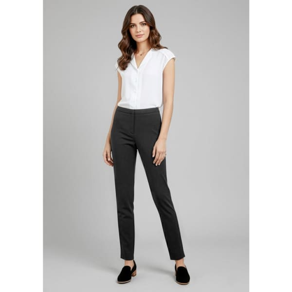 A woman wearing black slacks paired with a white blouse, standing confidently against a plain background.