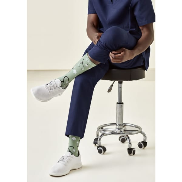 A pair of green unisex socks featuring a playful pattern, worn with white shoes and navy trousers.