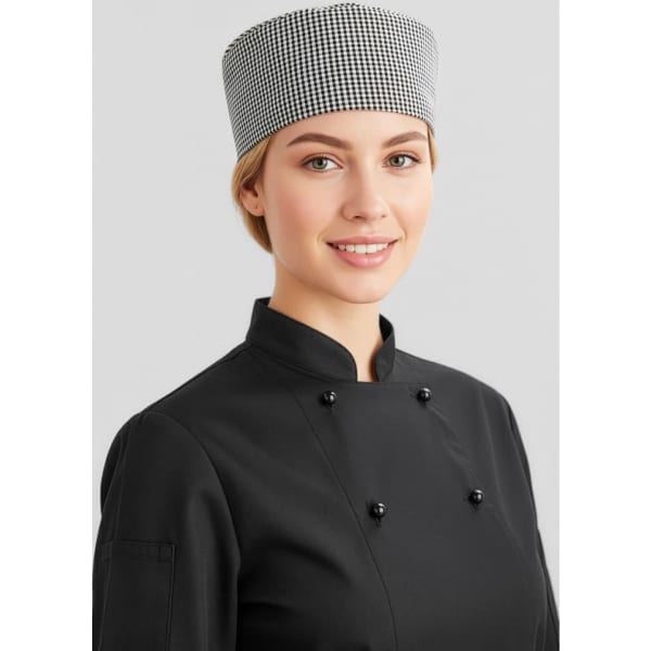 A female chef wearing a black chef jacket with buttons and a checkered hat, smiling at the camera.