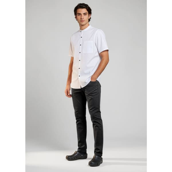 A man stands wearing black chef flex pants paired with a short-sleeve white shirt. The outfit includes a logo.