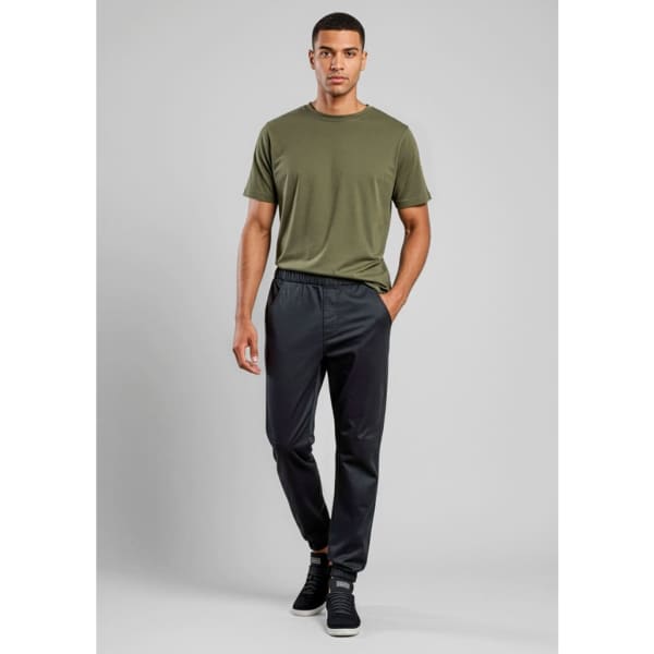 A man stands wearing olive green t-shirt and black jogger pants. The pants have an elastic waistband and a logo.