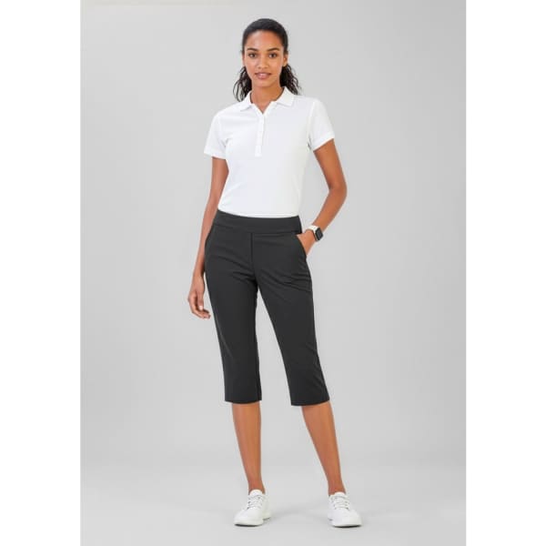 A woman poses wearing black 3/4 length stretch pants and a white polo shirt. The pants have a sleek design and pockets.